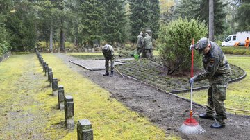 Männer reinigen eine Weg. Links davon eine Reihe Grabkreuze