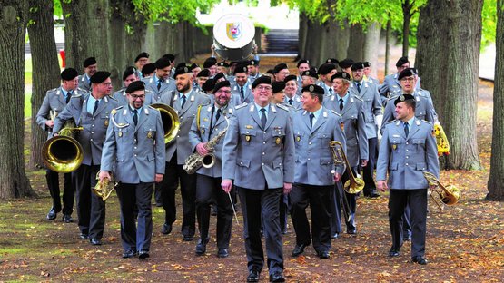 Eine Gruppe Menschen in Bundeswehruniform geht durch eine Allee. Sie halten verschiedene Musikinstrumente in den Händen.